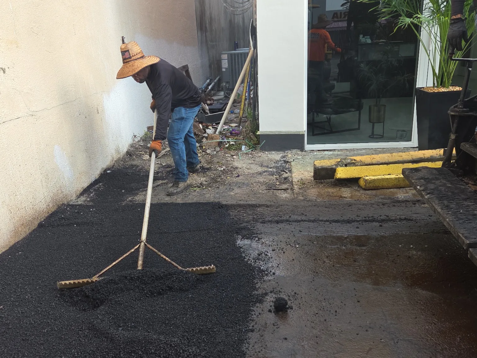 Crew member hand-raking fresh asphalt at an edge and transition